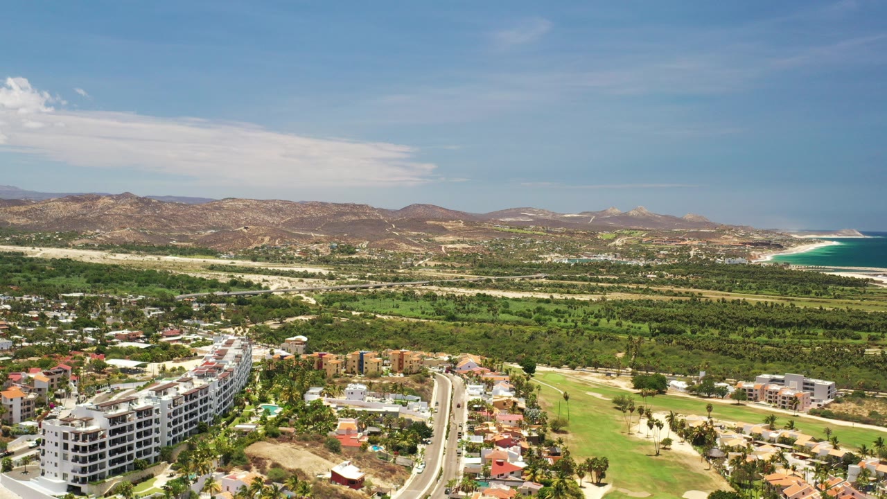 Aerial view of buildings, houses, green terrain, hills, and ocean coastline.