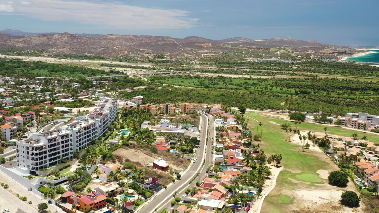 Aerial view of a sunny resort neighborhood, golf course, hills, and distant coast.