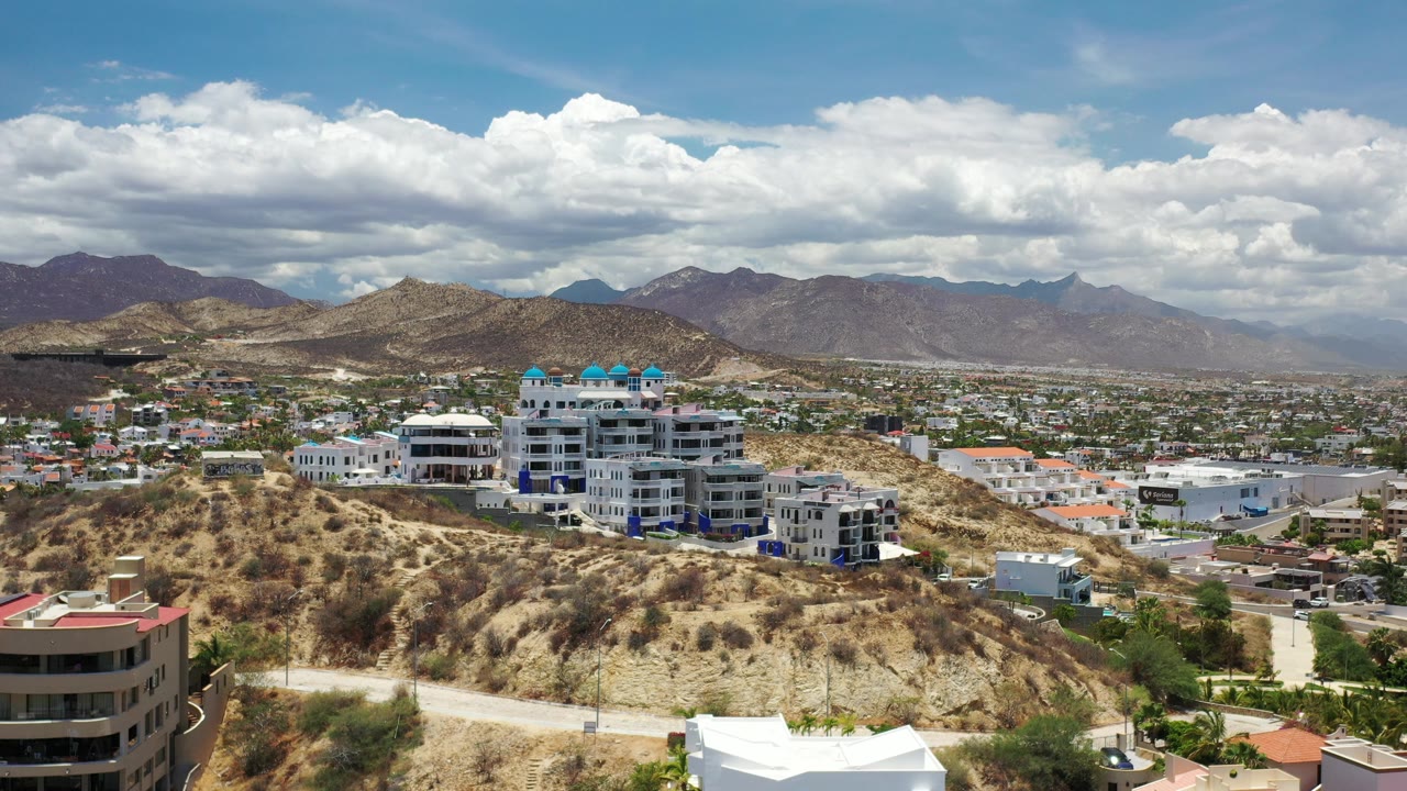Sunlit city and desert hills with white buildings and mountains behind.