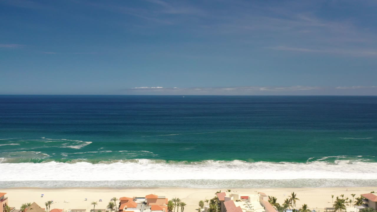 Blue-green surf rolling toward a pale beach from above.