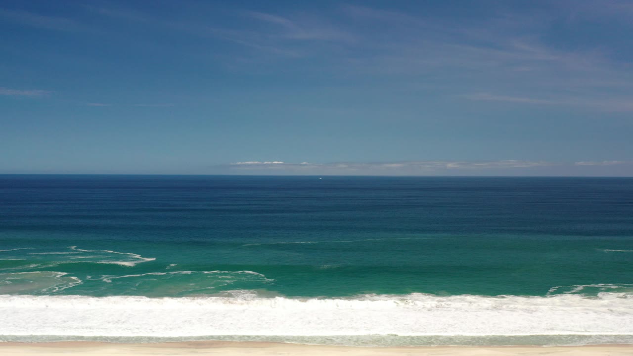 Opening frame of the Los Cabos, Mexico coastline with a level ocean horizon, blue-green water, white surf at the bottom edge, and no visible people.