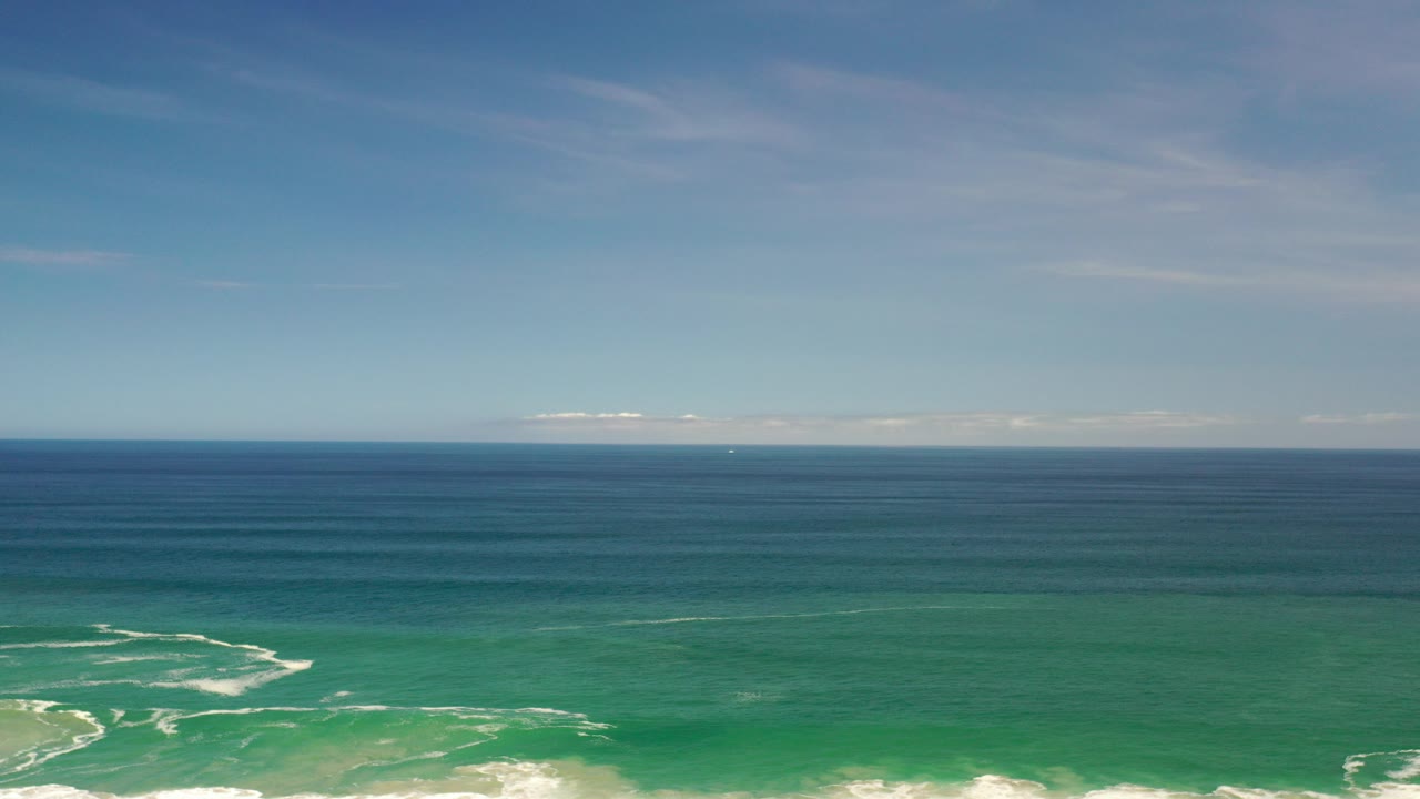 Aerial view over Los Cabos, Mexico water, with deep blue ocean near the horizon, green nearshore water below, white surf along the lower edge, and no visible people.