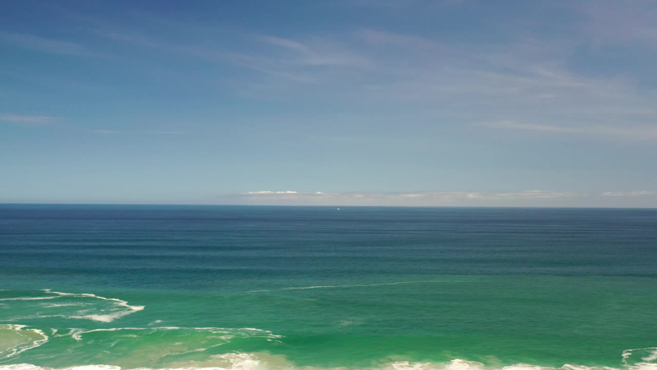 Wide aerial frame from Los Cabos, Mexico showing a straight ocean horizon, darker blue water in the distance, green water closer to shore, small white wave lines, and no visible people.
