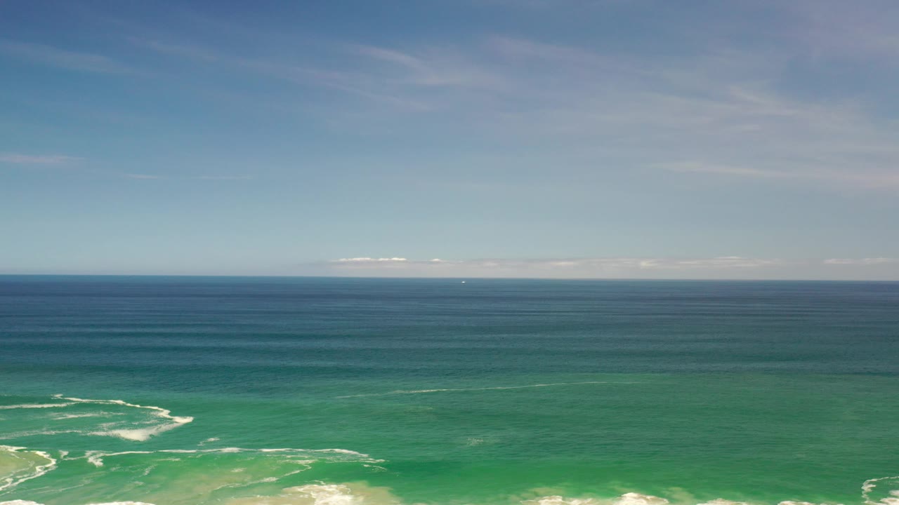 Turquoise-green ocean with white surf patterns beneath a blue horizon.