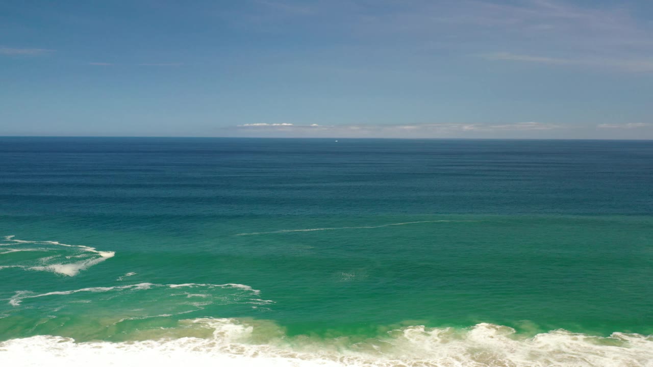 Los Cabos aerial frame with a white foam patch farther left in the water, surf at the lower edge, deep blue sea beyond, and no visible people.