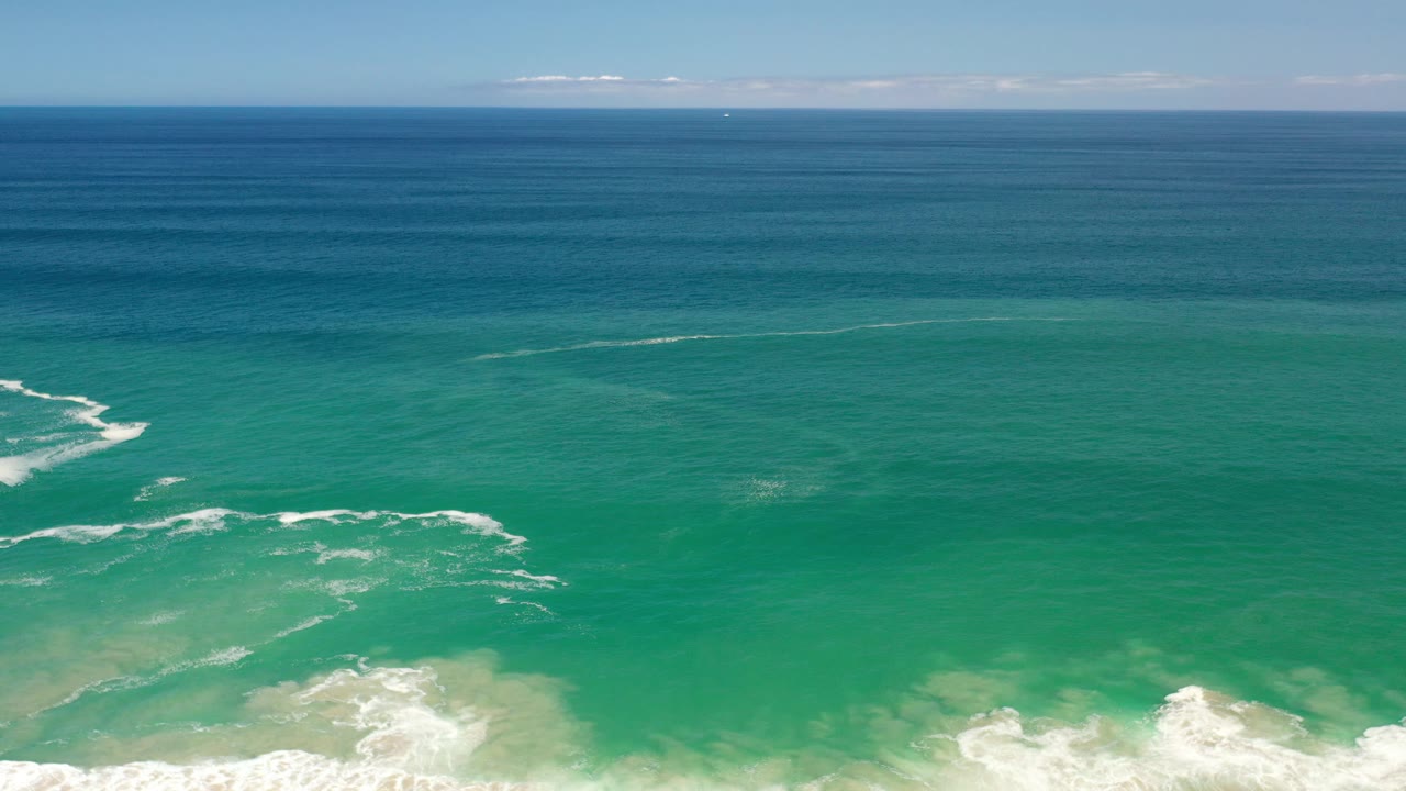 Open blue and green ocean with white surf patches and a level horizon.