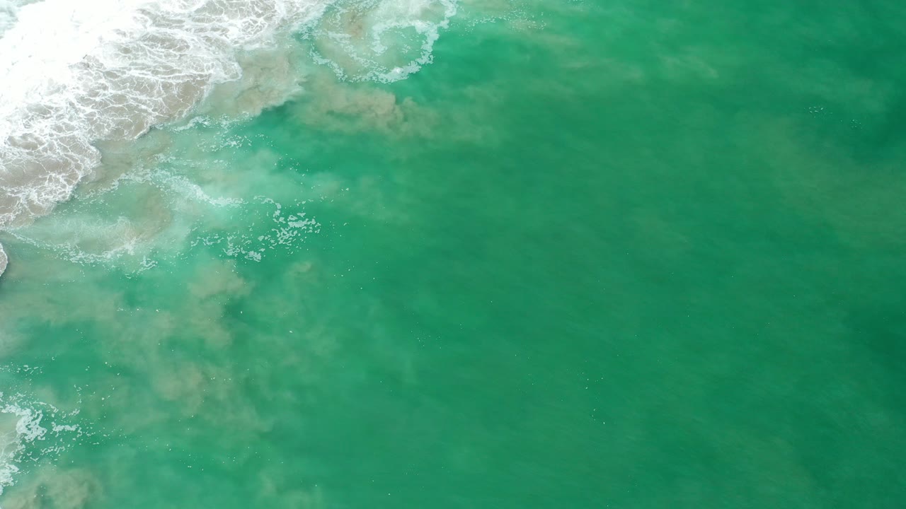 Overhead green surf water mixing with pale sand and white foam.