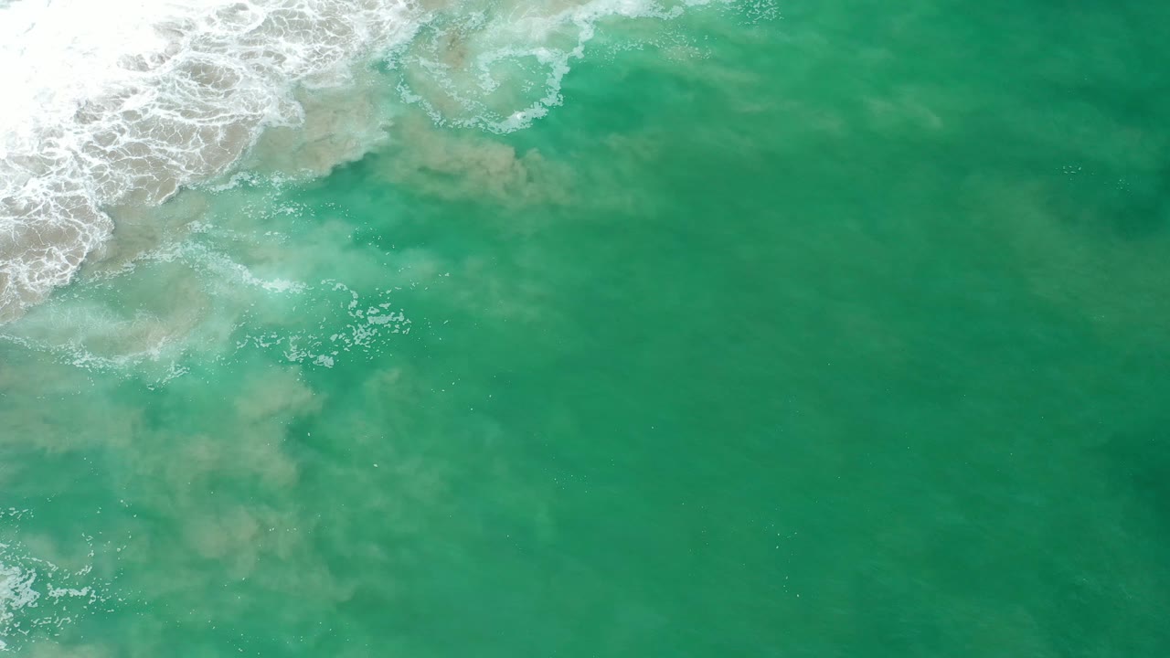 White surf edge over green water with suspended sand below.
