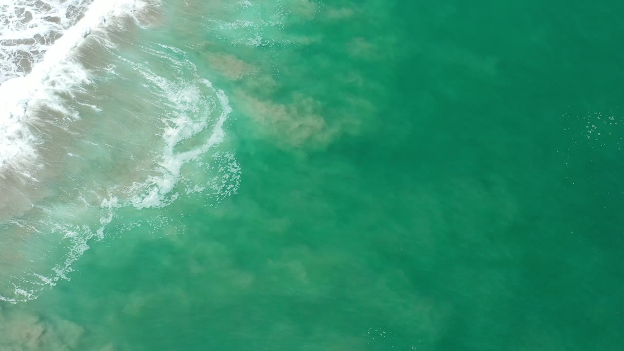Turquoise ocean surface with surf foam along the top left edge.