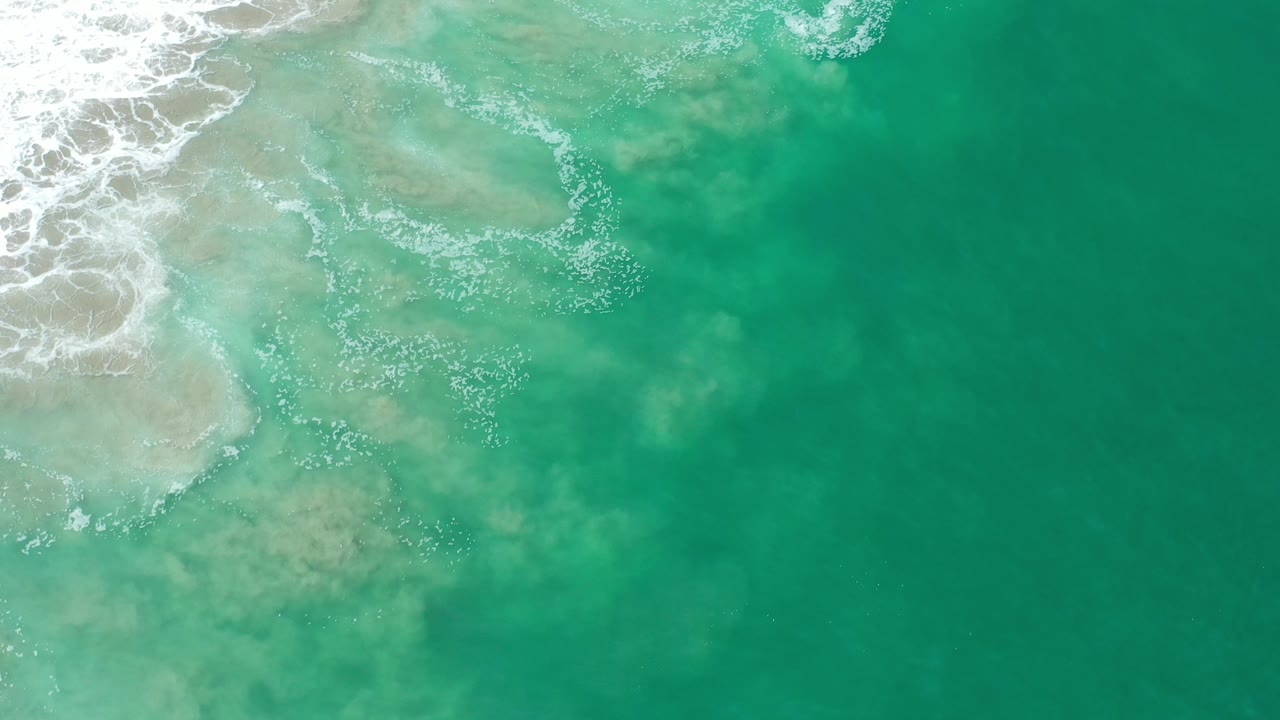 Green ocean water and white foam over shallow sand.