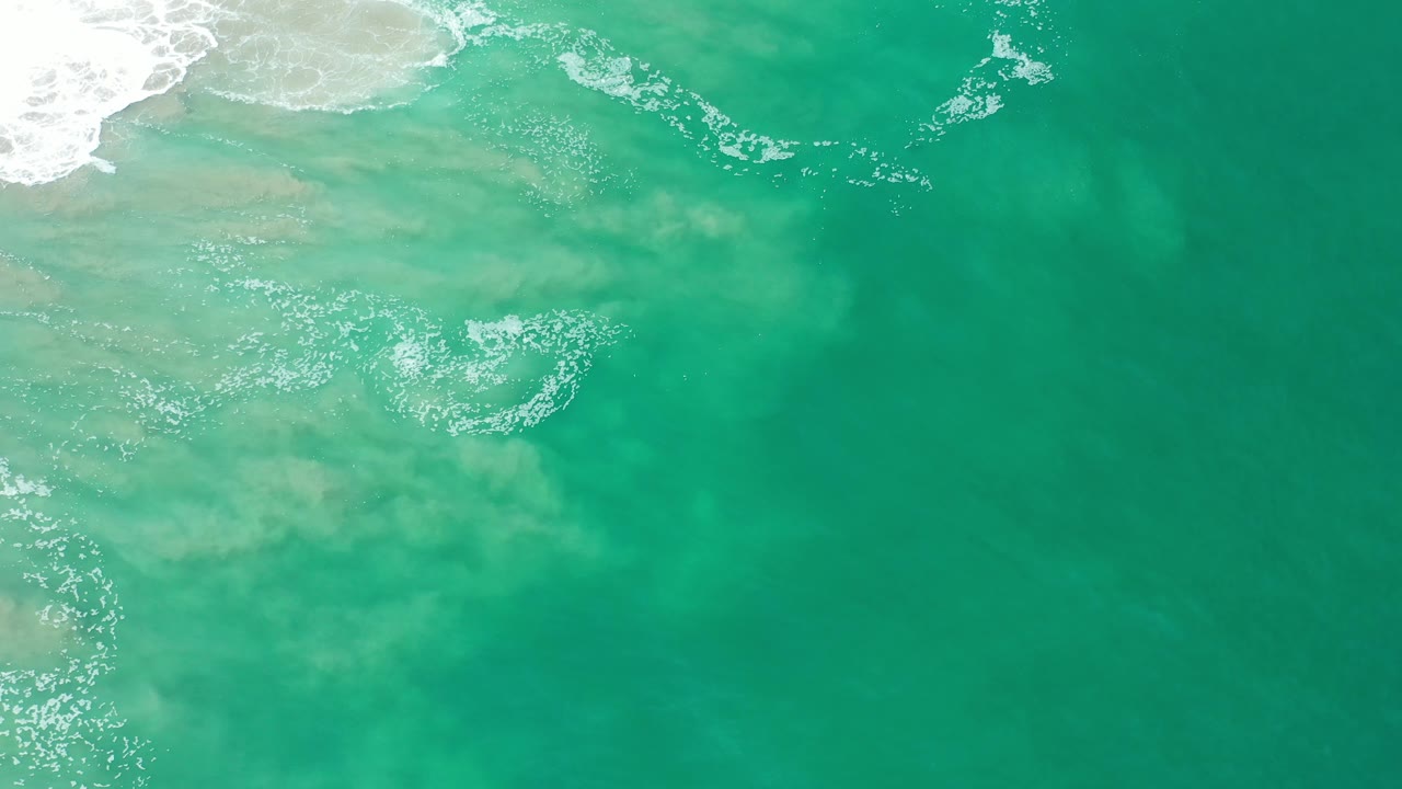 Open teal ocean surface with surf and foam near the top edge.