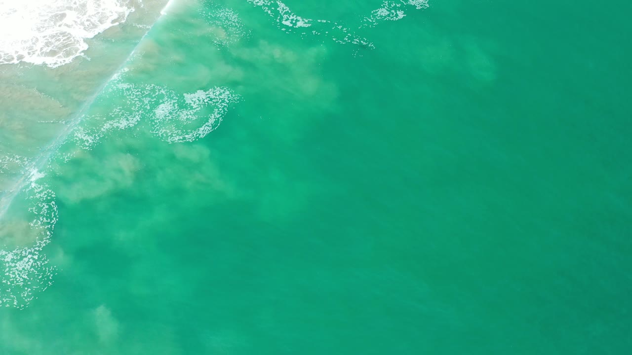 Overhead turquoise seawater meeting a sandy beach edge