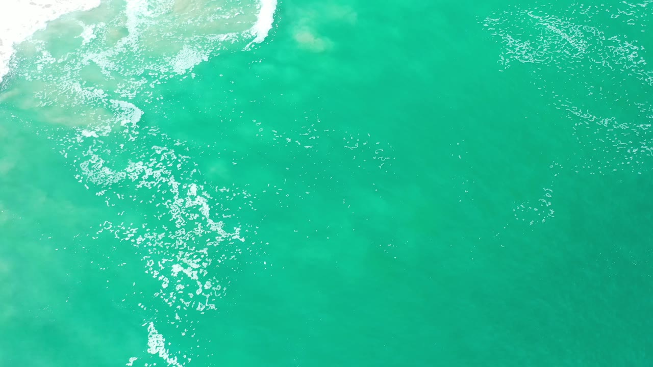 Turquoise ocean seen from above with sparse white foam and underwater color variation.