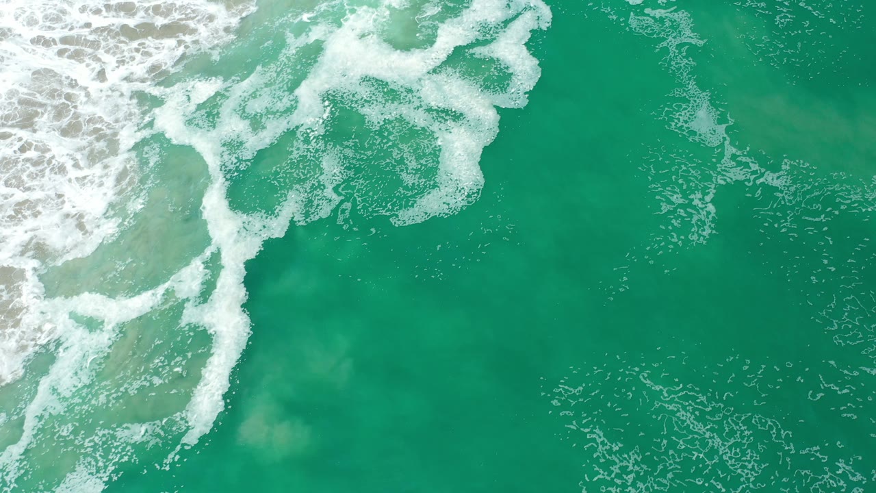Breaking surf forms white streaks over green-blue ocean water.
