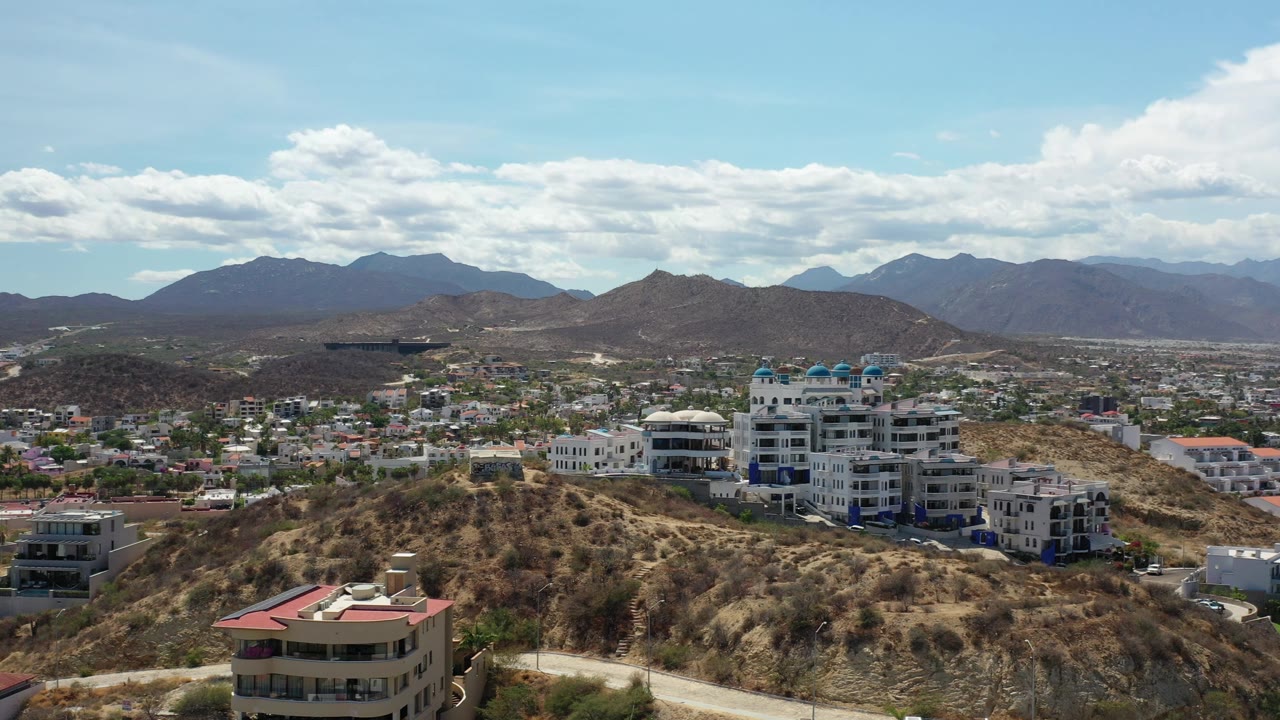 Elevated view of hillside buildings, town, mountains, and clouds.