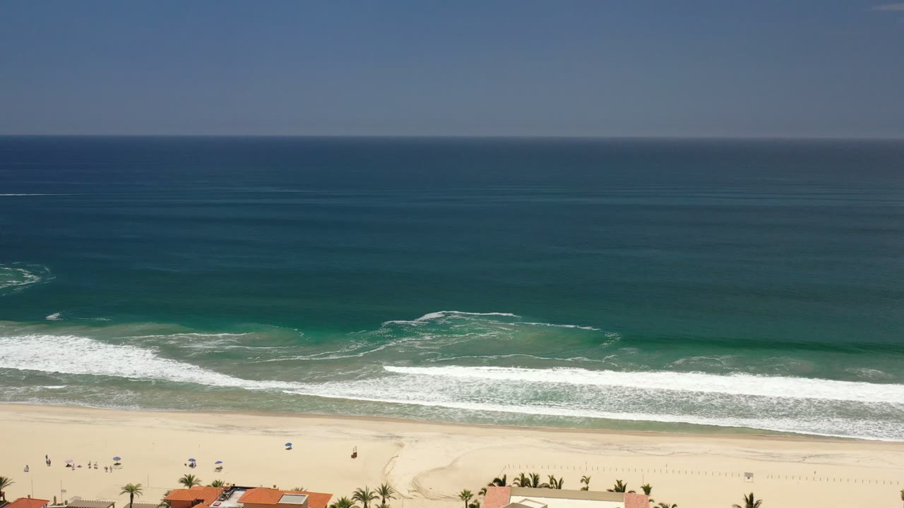Wide aerial view of ocean waves reaching a sandy beach.