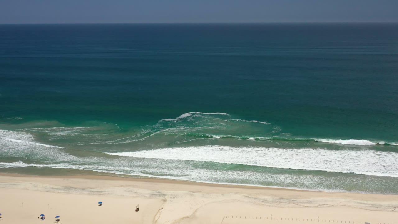 Wide aerial view of ocean waves breaking onto a sandy beach.