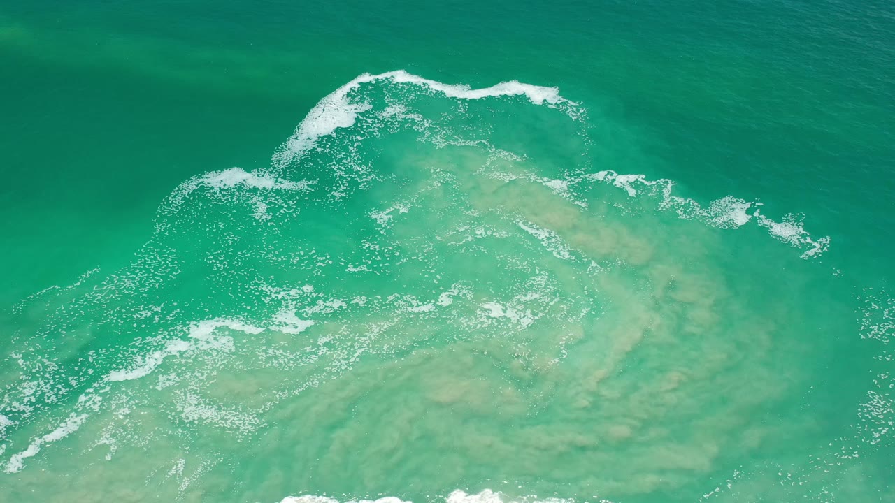 Aerial Los Cabos seawater frame with a wider white foam band near the top and pale green sand-toned water beneath, with no visible people.