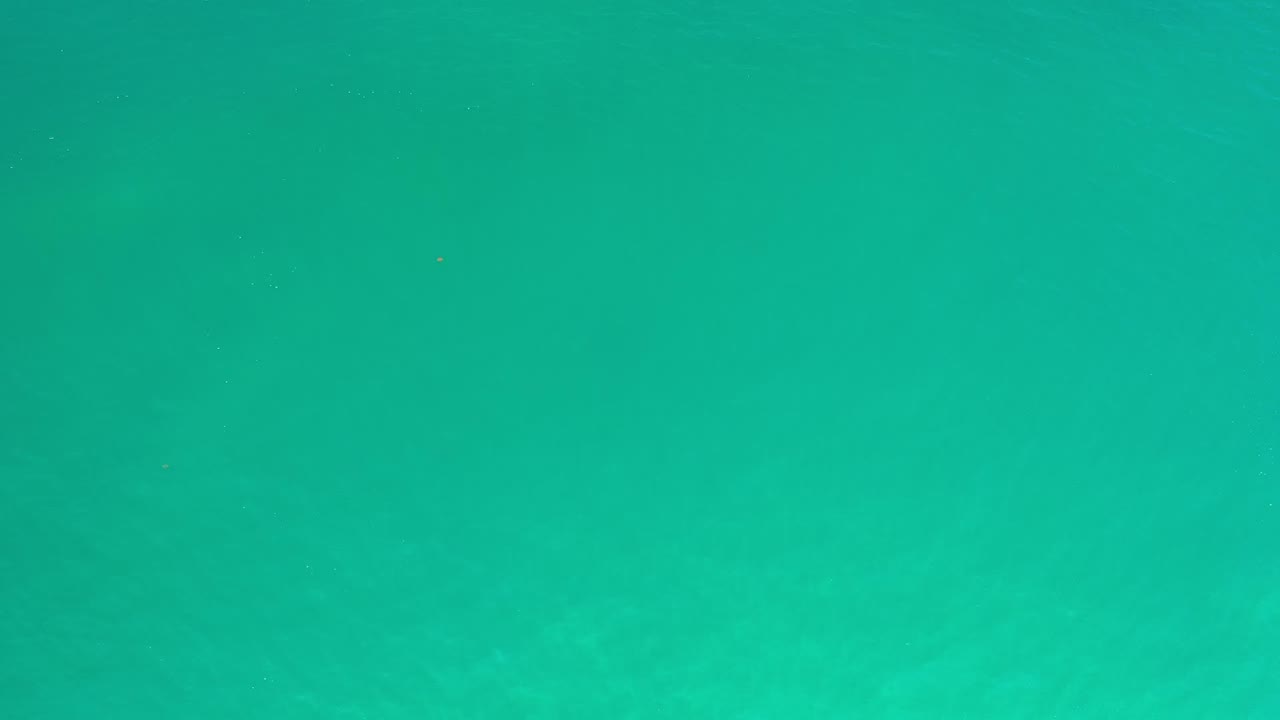 At one second, turquoise ocean water remains centered in frame with faint darker patches beneath the surface and no visible people.