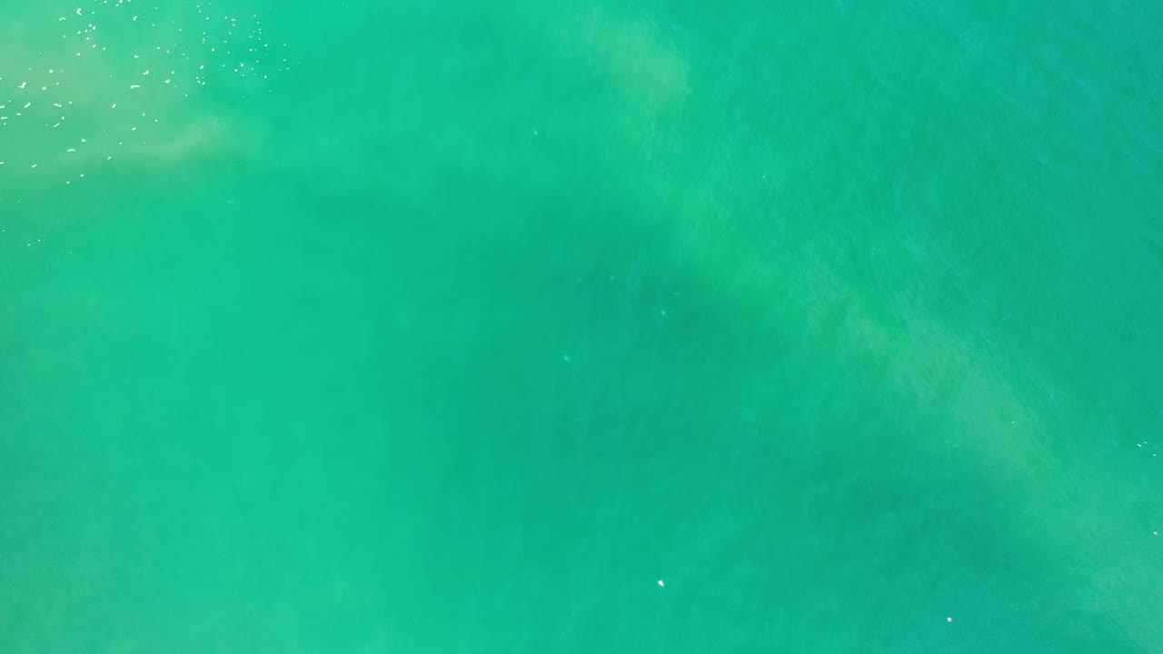 Overhead view of turquoise water in Los Cabos, Mexico, with faint pale foam patterns near the upper left and no visible people.