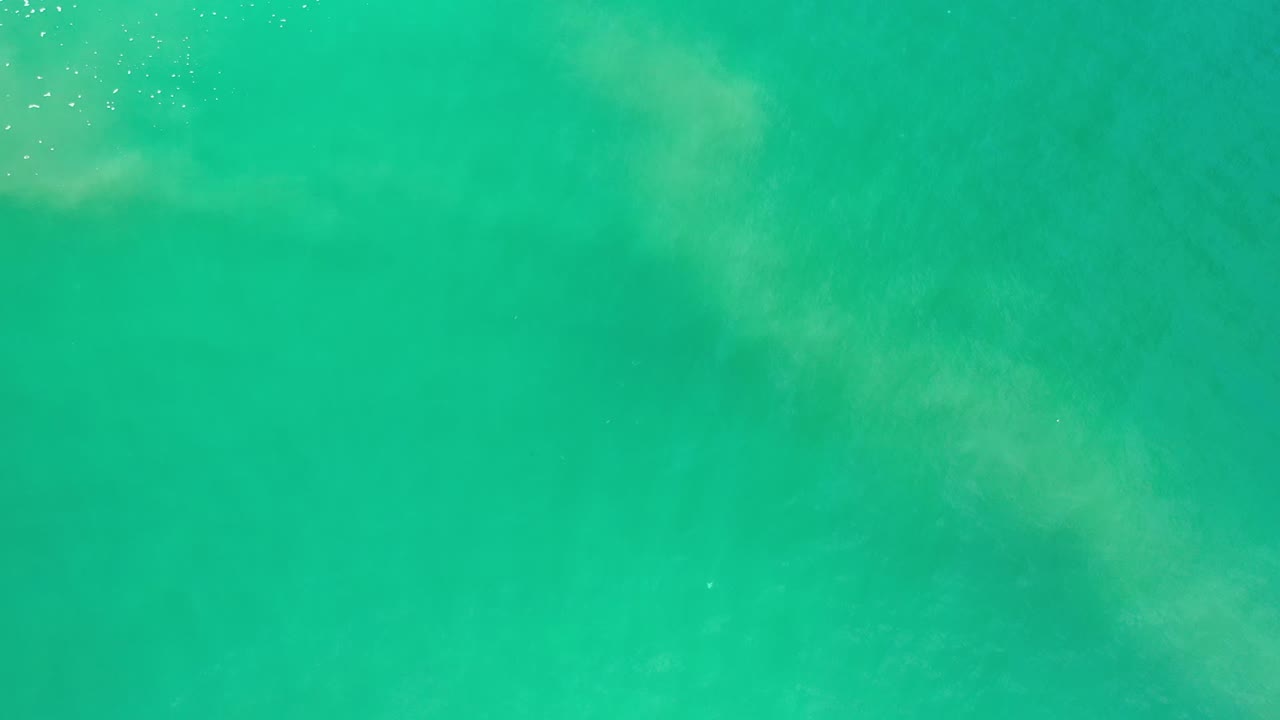 Turquoise ocean water in Los Cabos, Mexico shows faint foam and soft submerged sand shapes across the frame, with no visible people.