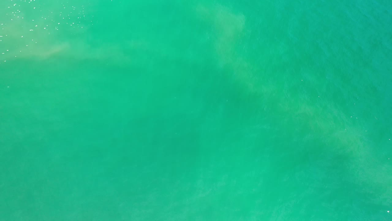 Aerial view of Los Cabos green ocean water with pale wave bands crossing the frame and no visible people.