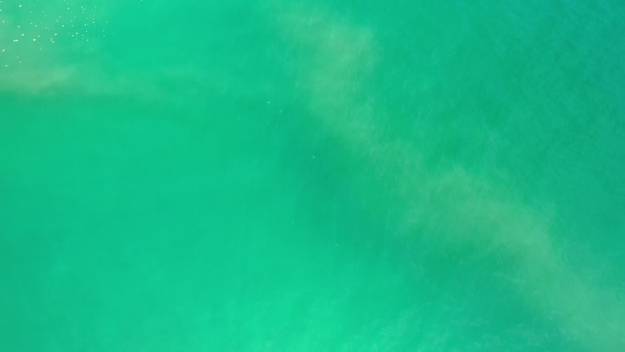 Turquoise green sea water with faint sediment clouds viewed from above.