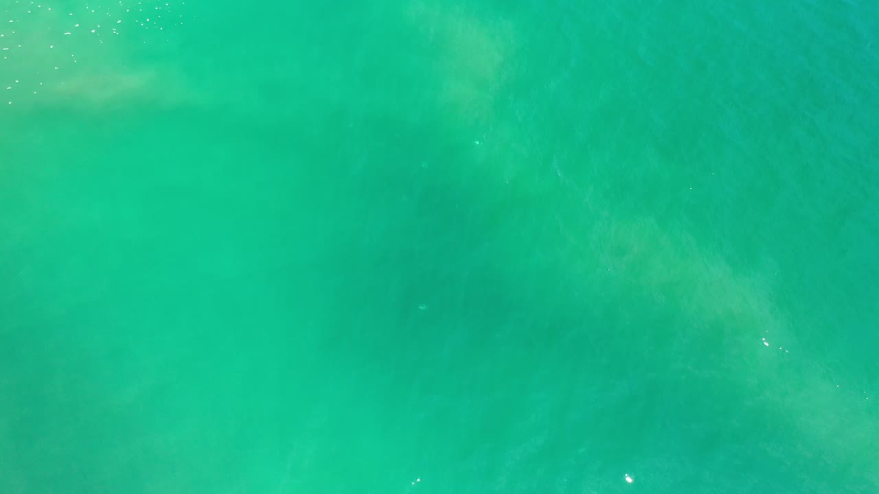 Blue-green ocean surface in Los Cabos, Mexico, with scattered sun sparkles and muted cloudy shapes under the water, no visible people.