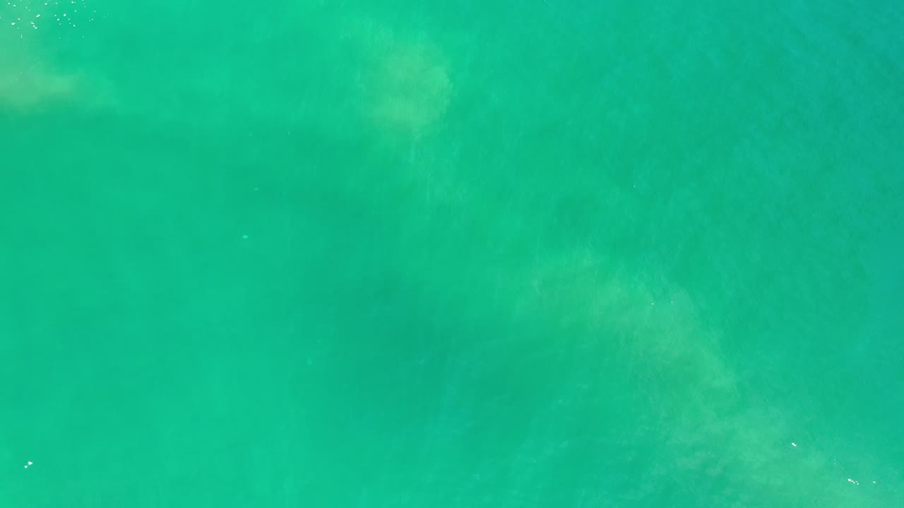 Early frame of Los Cabos water showing a smooth blue-green surface, slight ripple movement, one small sun glint, and no visible people.