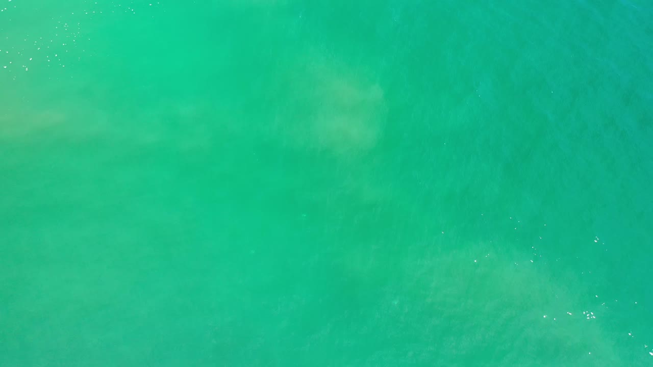 Turquoise Los Cabos ocean surface fills the frame, with diffuse lighter patches below the water and no visible people.