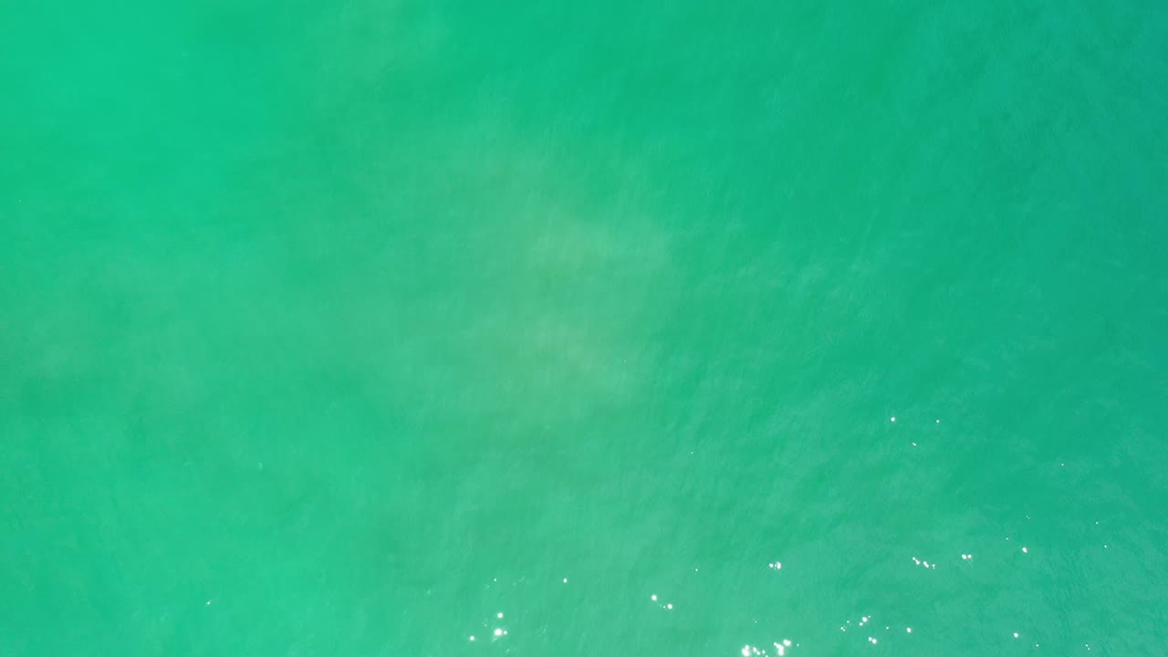 Overhead Los Cabos sea surface with blue-green color, scattered bright glints, and no visible people or shoreline.