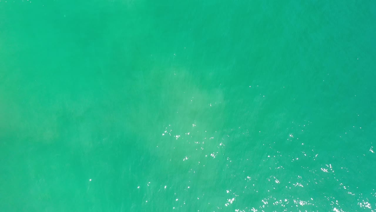 Straight-down view of green ocean water in Los Cabos, Mexico, with soft ripples and a small band of bright reflection low in frame, with no visible people.