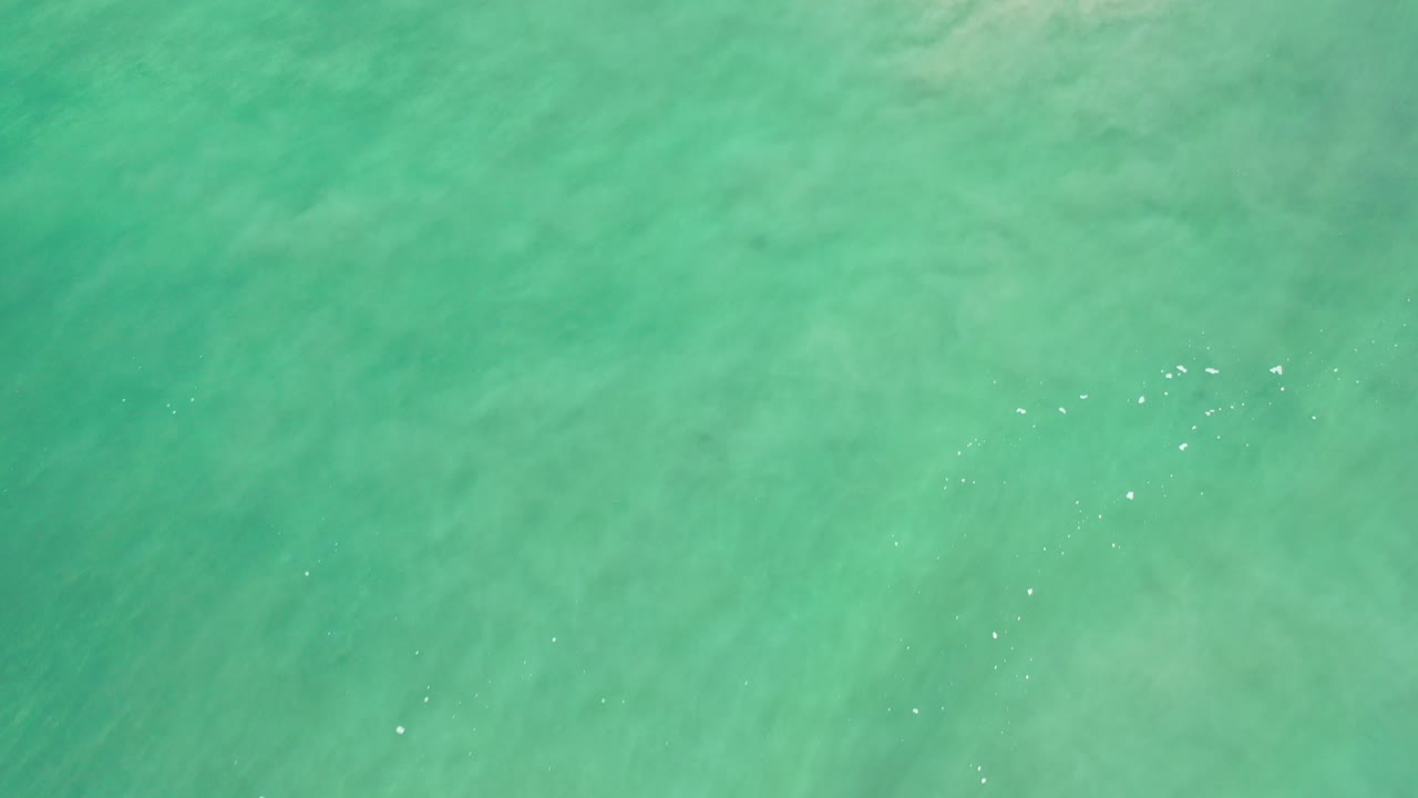 Overhead view of turquoise ocean water in Los Cabos, Mexico, with faint sandy patterns below the surface and no visible people.