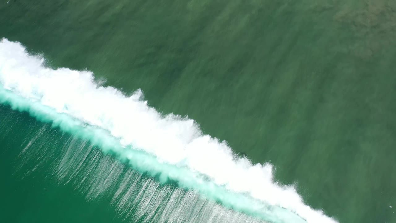 Aerial view of the foamy wave line stretching diagonally through green-blue ocean in Los Cabos, Mexico, with no visible people.