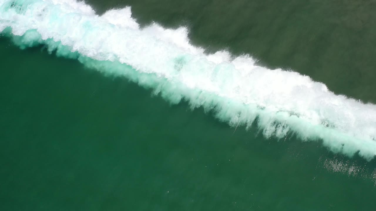 White surf breaks along the upper edge of green ocean water.