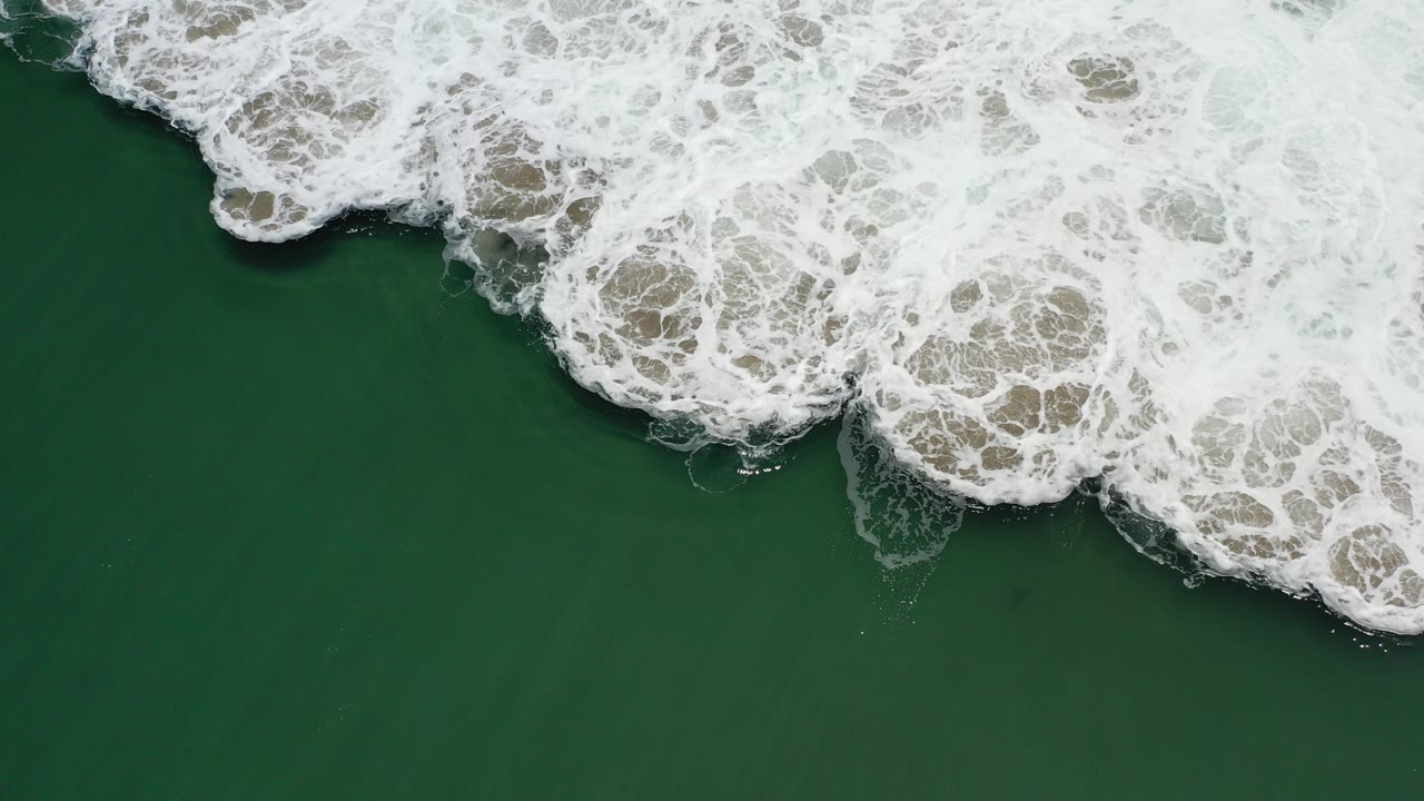 Overhead view of green ocean water in Los Cabos, Mexico, with thick white surf curling across the top of the frame and no visible people.