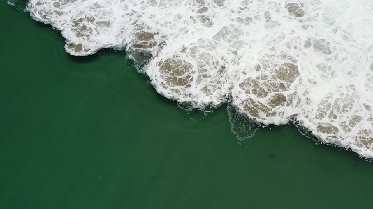 Overhead ocean water with dense surf foam across the top and right.