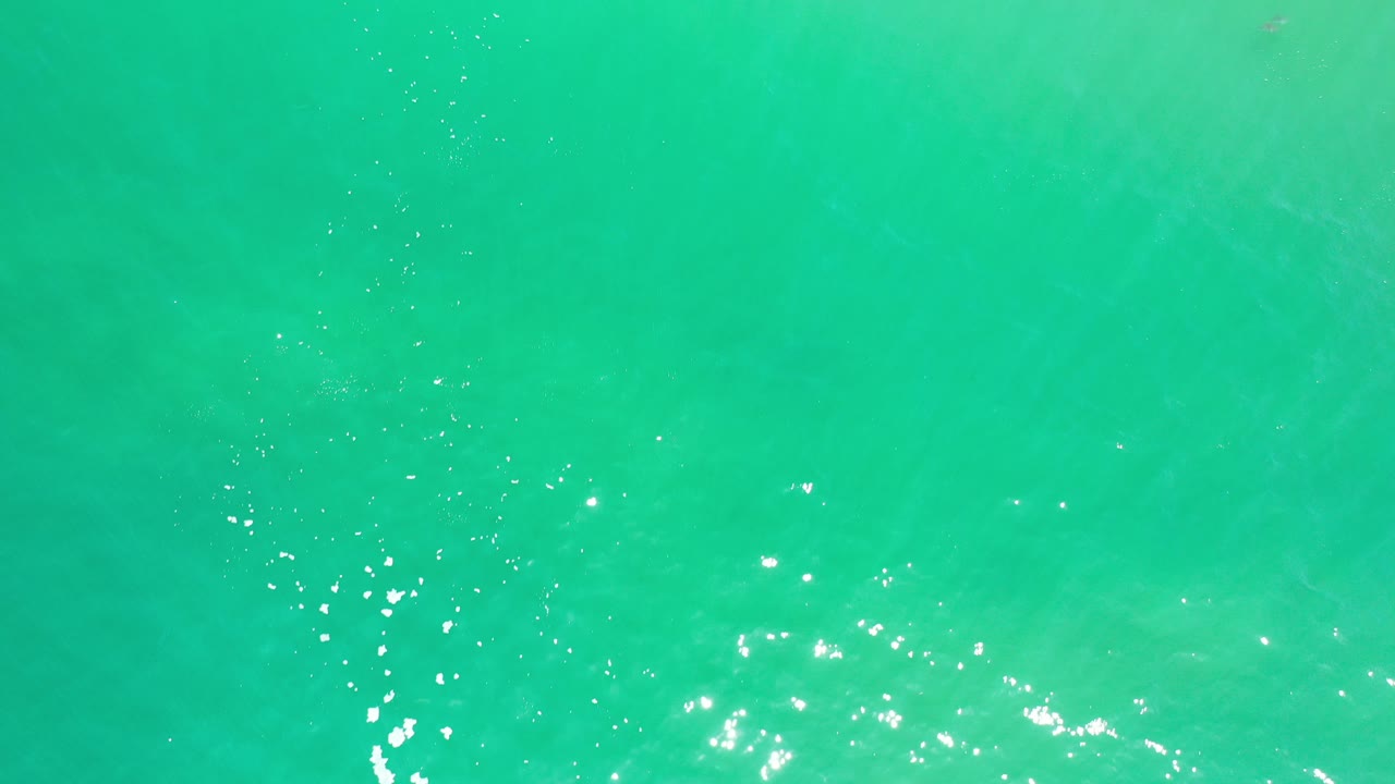 Overhead view of greenish blue seawater in Los Cabos with bright sun glints near the lower left and no visible people.