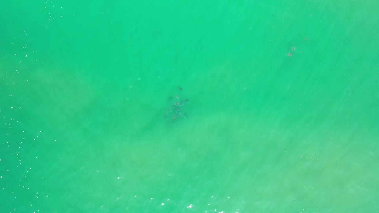 Turquoise sea seen from above with scattered white glints and a shadowed area.