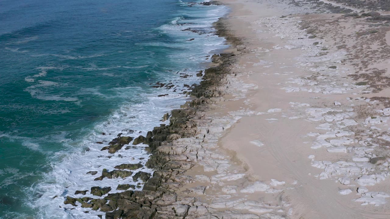 Surf line and exposed rocks run diagonally along an empty beach.