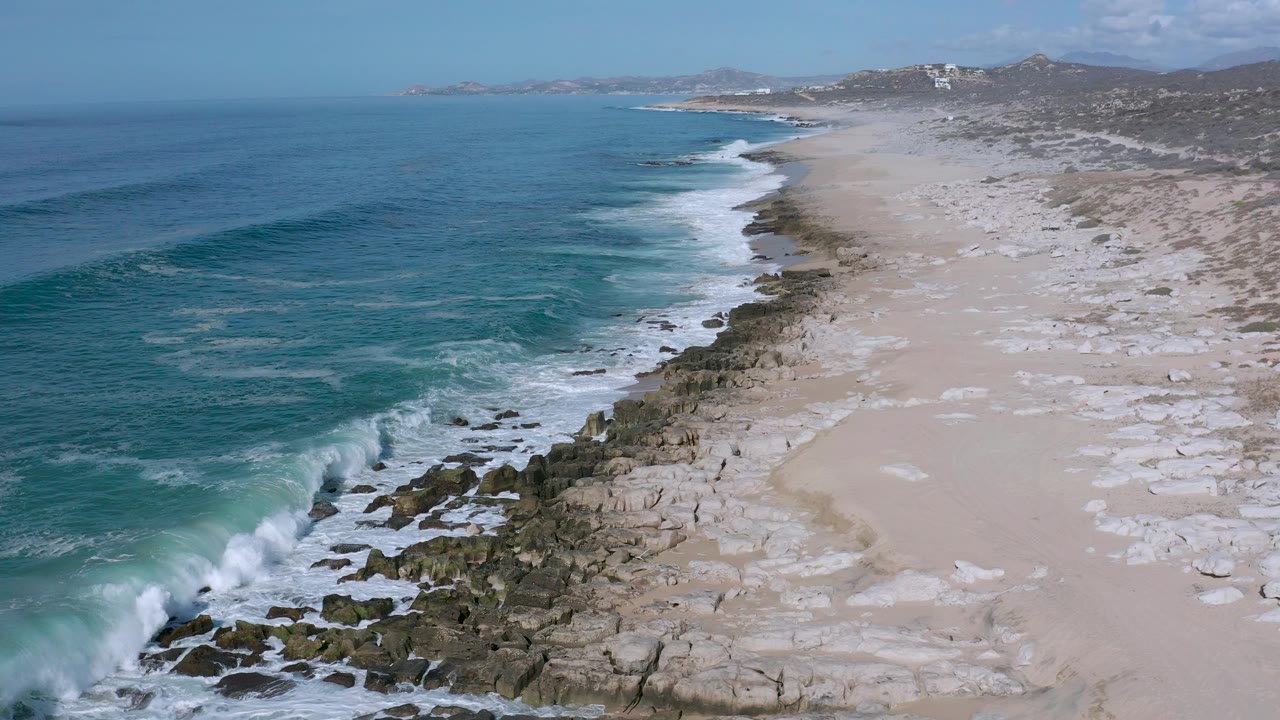 Aerial view of blue ocean waves beside a sandy rocky beach.