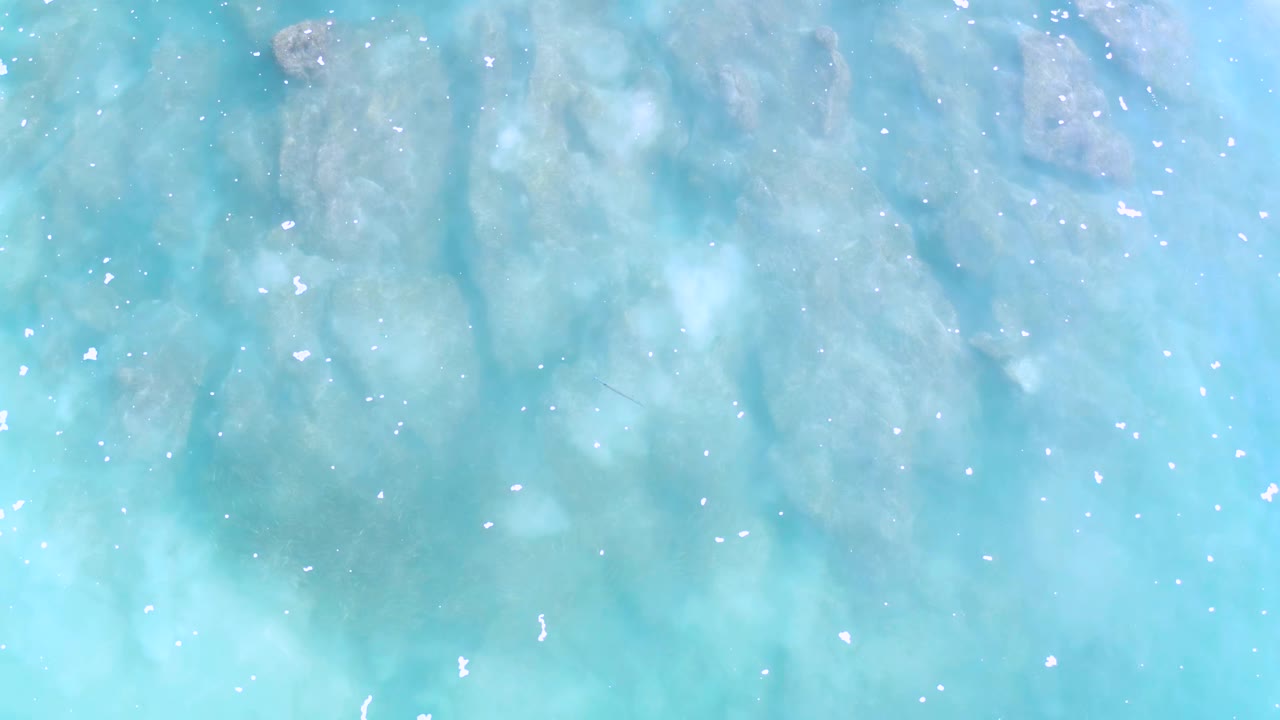 Blue-green shallow water in Los Cabos, Mexico, shows soft ripples over pale submerged reef, with no visible people or vessels.