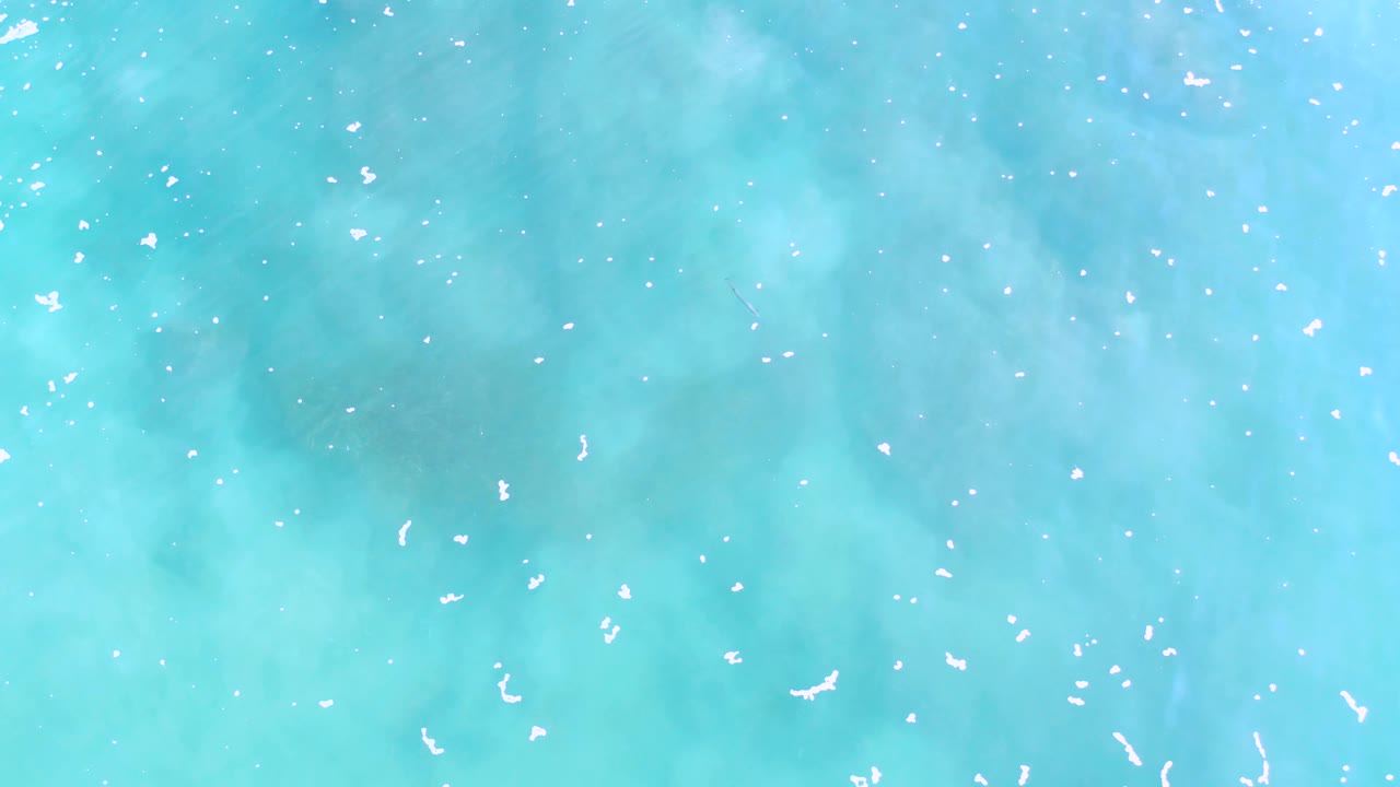 Top-down Los Cabos sea surface with small white ripples over cloudy teal water and no visible people.