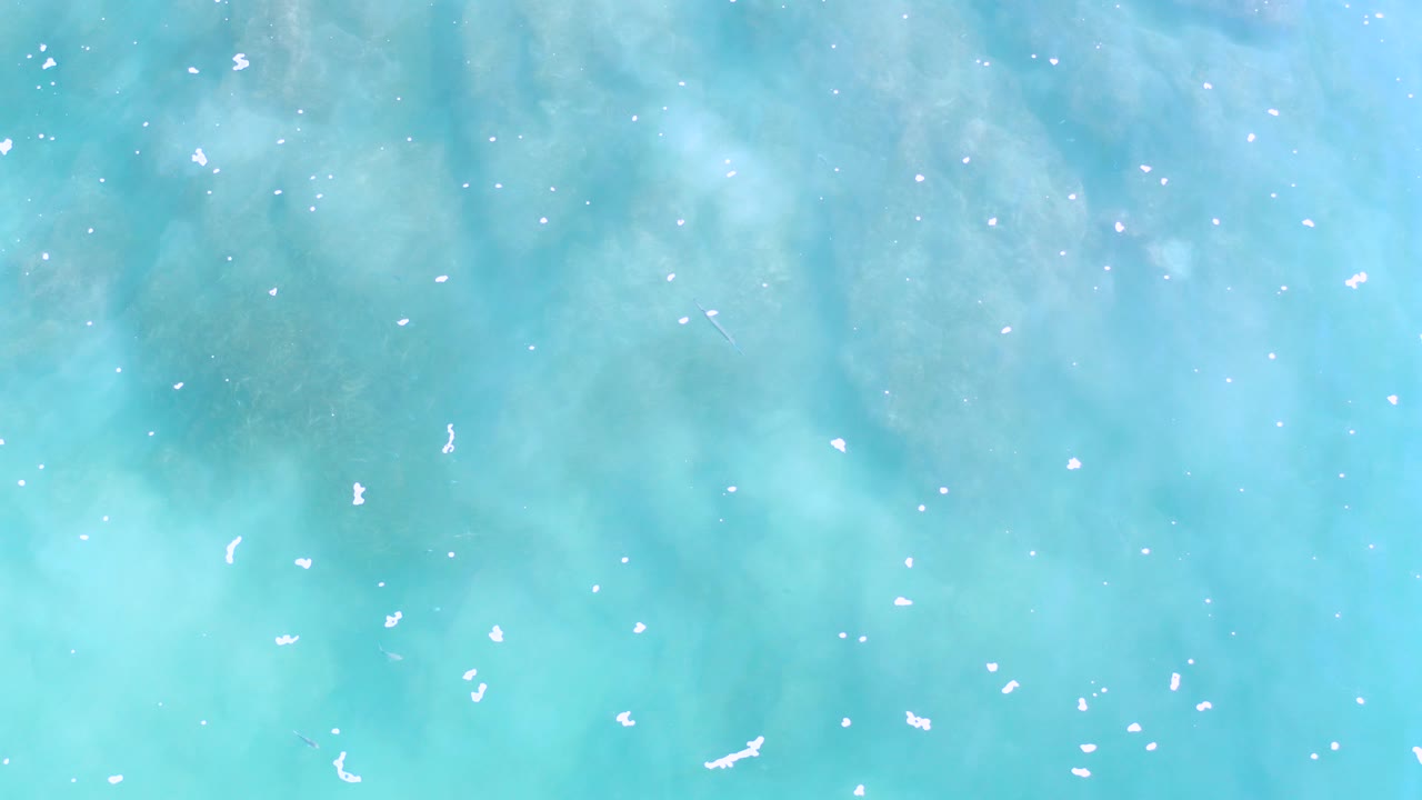 Overhead turquoise sea with scattered white foam flecks.