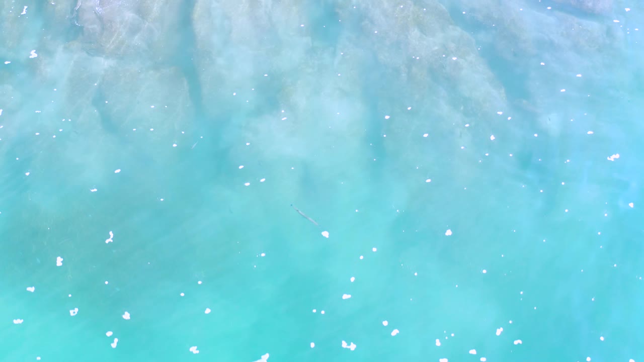 Top-down Los Cabos ocean water with milky aqua color, faint darker patches under the surface, small white foam marks, and no visible people.