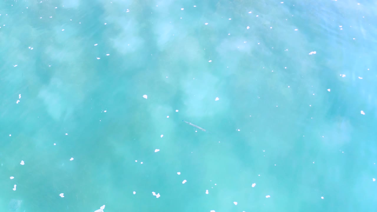 Turquoise ocean water in Los Cabos appears from above with brighter foam marks across the middle of the frame and no visible people.