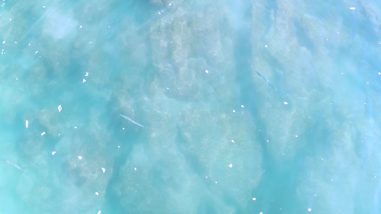 Straight-down view of pale turquoise ocean in Los Cabos, Mexico, with scattered foam-like points, soft cloudy color bands, and no visible people.