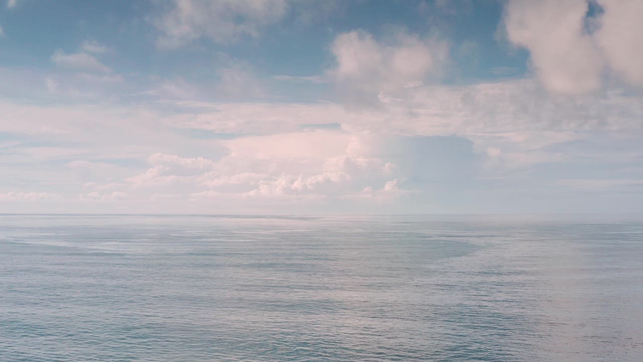 Wide Los Cabos ocean view with a straight horizon, soft blue water, pale cloud reflections, and no visible people.