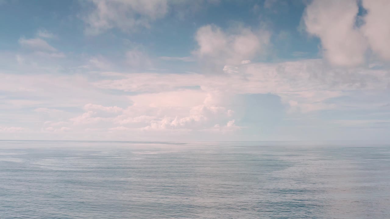 Calm blue ocean sits below a broad cloud bank in Los Cabos, with a low horizon and no visible people.