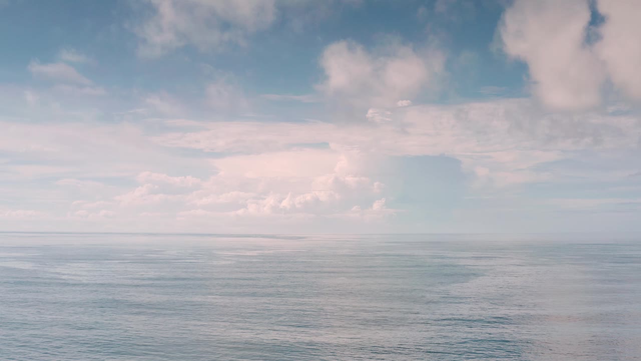 Open Los Cabos water stretches to a distant horizon beneath scattered pale clouds, with no visible boats or people.